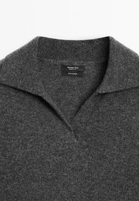 Maglione grigio in cashmere con scollo a V e colletto ampio. Presenta una texture sottile e include un'etichetta nera con informazioni sul marchio e sul materiale.