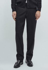 Donkergrijs op maat gemaakte broek van een stevige stof met een rechte pijp. Gekleed met zwarte instappers, wat zorgt voor een nette, klassieke uitstraling.