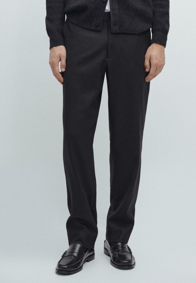 Donkergrijs op maat gemaakte broek van een stevige stof met een rechte pijp. Gekleed met zwarte instappers, wat zorgt voor een nette, klassieke uitstraling.