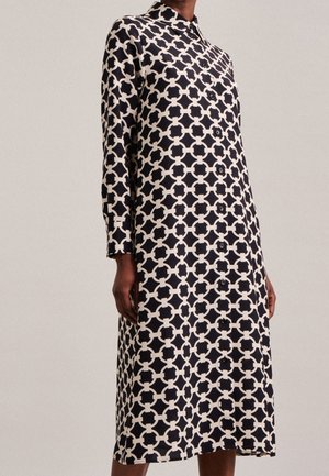 Sukienka zapinana na guziki, wykonana z lekkiego materiału, z czarno-kremowym geometrycznym wzorem, długimi rękawami i kołnierzykiem.