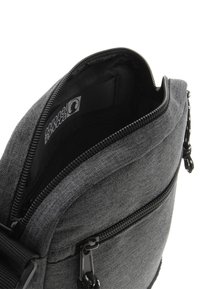 Bolso de hombro de tela gris con un compartimento principal con cremallera, exterior texturizado y forro interior negro. Presenta una etiqueta con el logo en el interior.