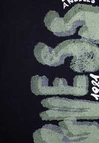 T-shirt en coton noir avec un grand graphisme de coup de pinceau vert texturé et le texte "Los Angeles" en blanc, mettant en avant un design d'impression audacieux.