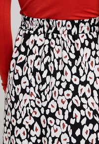 Černá sukně s bílým a červeným leopardím vzorem, vybavená elastickým pasem a splývavou texturou látky.