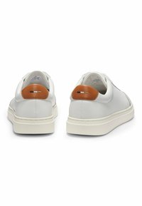 Valkoiset nahkakengät teksturoidulla pinnalla, minimalistinen muotoilu, kontrastiväriset ruskeat kantapääkoristeet ja pyöristetty kumipohja.