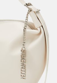 Cream-colored leather bag with a smooth texture, zip closure, and a silver chain accent featuring the brand name in bold lettering.
