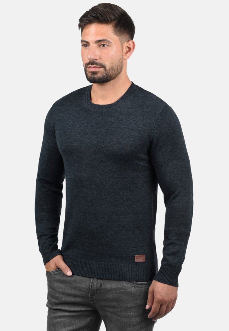 Dark blue, long-sleeved sweater made of knit fabric. Features a round neckline and ribbed hem, with a small brand patch at the waist.