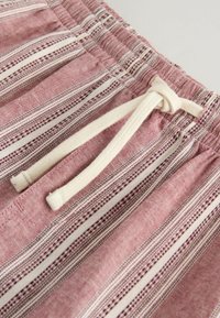 Gros plan sur un short en tissu à rayures roses et blanches, avec une taille élastique et un cordon de serrage crème noué.