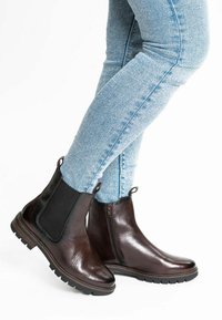 Osoba nosząca jasnoniebieskie skinny jeansy oraz ciemnobrązowe skórzane botki Chelsea z elastycznymi bokami i bocznym zamkiem błyskawicznym.