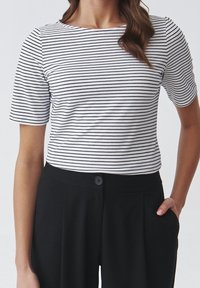 Top de manga corta a rayas en blanco y negro, con cuello redondo y ajuste ceñido, combinado con pantalones negros de cintura alta con cierre de botón.