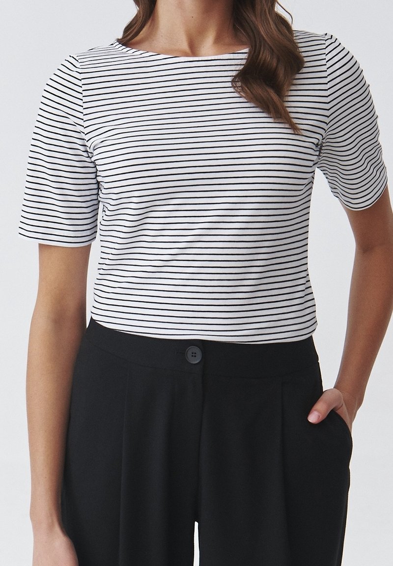 Top de manga corta a rayas en blanco y negro, con cuello redondo y ajuste ceñido, combinado con pantalones negros de cintura alta con cierre de botón.