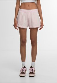 Shorts en coton rose avec une taille élastique, présentant une coupe décontractée et un ourlet cousu. Portés avec des chaussettes blanches et roses superposées et des baskets.