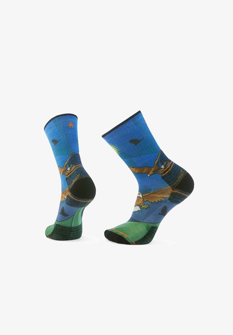 Calcetines coloridos que presentan un paisaje azul y verde con aves y montañas. Hechos de tela con un talón y punta reforzados en negro.