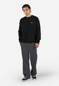 Fekete, hosszú ujjú kötött pulóver texturált kivitelben, szürke, bő szárú nadrággal és krémszínű részletekkel díszített fekete tornacipőkkel párosítva.