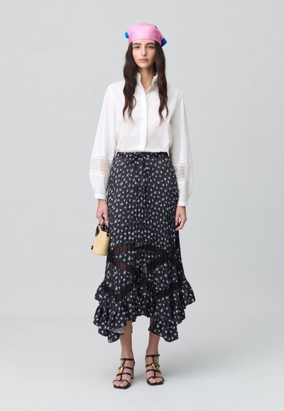 Blusa blanca con mangas acampanadas, falda midi negra con estampado floral y detalles transparentes y volantes, pañuelo rosa en la cabeza y un pequeño bolso de rafia.