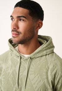 Felpa con cappuccio verde chiaro con motivo testurizzato, coulisse e finitura in tessuto morbido. Scollo rotondo sotto il cappuccio.