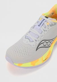 Sapatilha de corrida cinza com parte superior em malha, logótipo preto, atacadores brancos e sola colorida com detalhes em amarelo neon e laranja. Superfície texturizada.