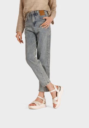 Jeans in denim grigio chiaro con taglio dritto, abbinati a sandali con cinturini color crema dotati di suola platform e leggere rifiniture metalliche.