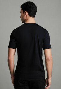 Tricou scurt cu mânecă neagră, din bumbac, cu guler rotund și o formă ajustată, cu o textură netedă și fără modele sau accente vizibile.