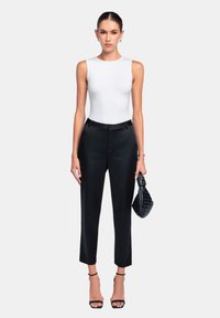 Weißer ärmelloser Bodysuit, schwarze maßgeschneiderte Hose mit Slim Fit und schwarze geflochtene Clutch. Dünne Riemchen-Heels runden den Look ab.