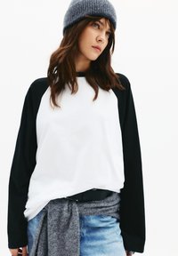 Hvid og sort langærmet skjorte med rund hals; parret med en grå strikket hue og en grå sweater bundet om taljen.