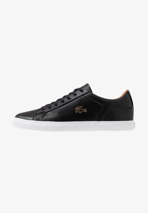 Black low-top leather sneaker with black laces, white sole, tan interior lining, and gold crocodile logo on the side.