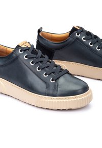 Baskets en cuir bleu foncé avec des semelles en caoutchouc beige, bout rond, œillets en métal et lacets. Fini lisse avec des accents de coutures.