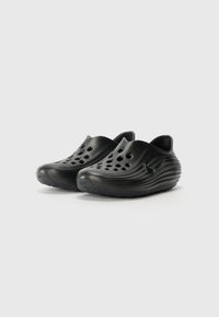 Black clogs made of smooth, flexible material with multiple ventilation holes and a ridged design; curved shape with a side logo accent.