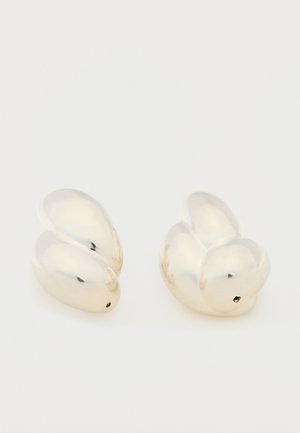 Pari kiiltäviä, sileitä hopeisia korvakoruja, jotka on muotoiltu abstrakteiksi, pyöristetyiksi kukkaniityn terälehdiksi ja esitetty valkoista taustaa vasten.