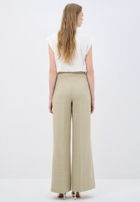 Beige wijde broek van textuurstof, met een hoge taille en subtiele plooien. Gecombineerd met een witte top met korte mouwen.
