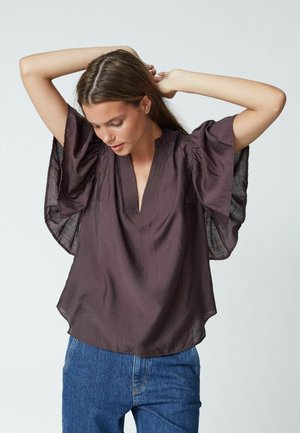 Dark purple top with wide, flared sleeves and a V-neckline, made of lightweight fabric with a subtle texture. Paired with blue jeans.