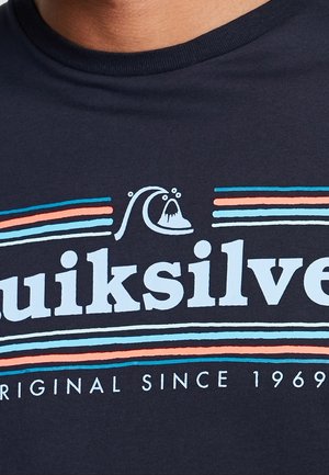 Ciemnoniebieska koszula z napisem "Quiksilver", logo fali powyżej oraz wielokolorowymi poziomymi paskami w kolorach pomarańczowym, niebieskim i jasnoniebieskim, z datą "Original since 1969."