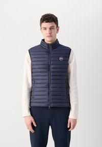 Vesta din material navy albastru, căptușită, cu fermoar în față, guler înalt și buzunare laterale, având un patch cu logo în apropierea pieptului stâng.