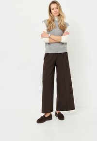 Grauer ärmelloser Pullover über einem cremefarbenen Rollkragenpullover, braune weit geschnittene Hose und dunkelbraune Loafers. Einfaches Design mit bequemer Passform.