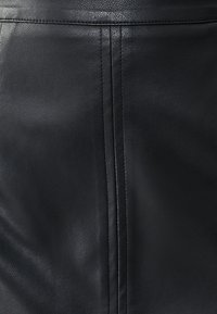 Čierna kožená sukňa s hladkou textúrou, so švovými detailmi behúcimi vertikálne a priliehavým strihom.