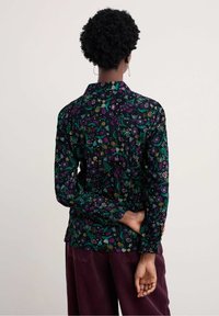 Camicia a maniche lunghe con bottoni in tessuto scuro, caratterizzata da un vivace motivo floreale. Tessuto liscio con una vestibilità comoda e colletto.