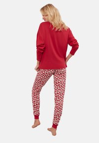 Czerwony top z długim rękawem w połączeniu z dopasowanymi spodniami w białe serca. Ubranie wykonane jest z miękkiego materiału z elastycznymi mankietami przy kostkach.