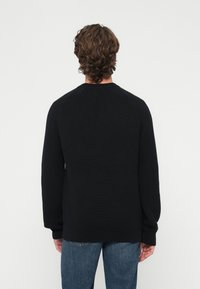 Pulover negru tricotat cu textură reiată, decolteu rotund și mâneci raglan, asortat cu blugi albaștri deschiși cu aspect uzat.