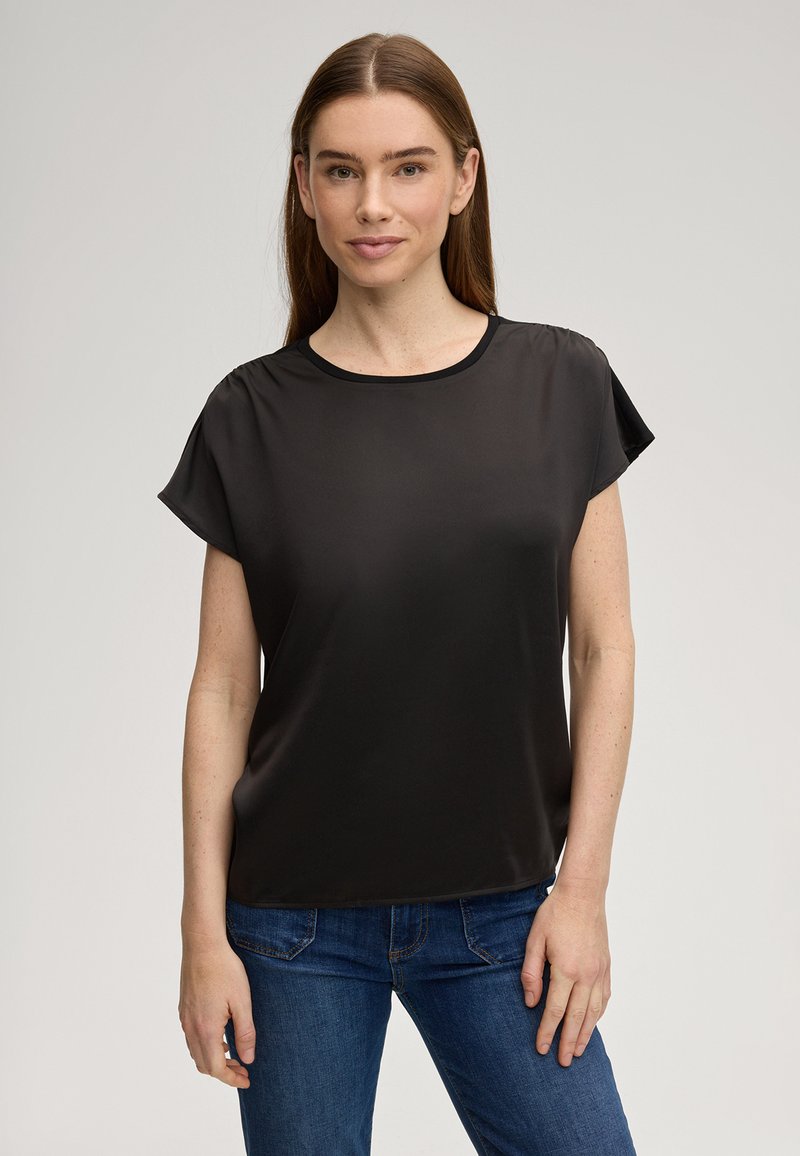 Top nero a maniche corte in materiale liscio e leggero, con collo arrotondato e vestibilità morbida. Presenta un design minimale senza motivi visibili.