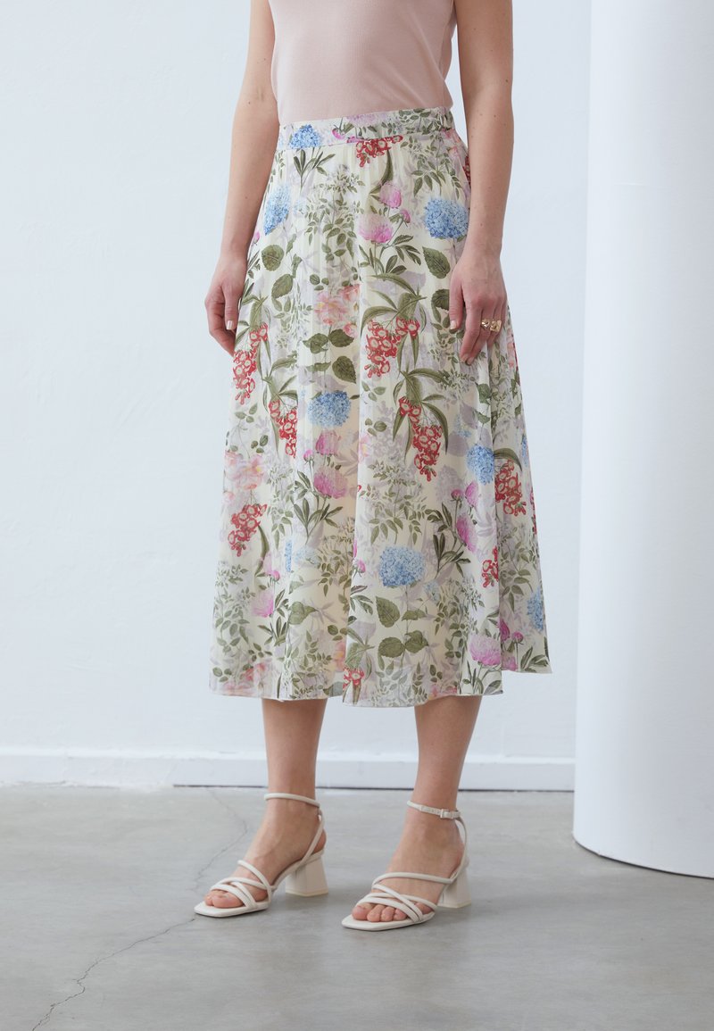 Floral midi skirt in cream, featuring various colored flowers, green leaves, and an elastic waistband. Paired with white strappy block-heel sandals.