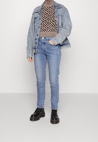 Veste en jean bleu clair, pull côtelé ajusté avec motif géométrique noir, jean taille haute bleu, et bottes de combat à lacets noires.
