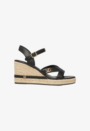 Sandale compensée en cuir noir avec bride à la cheville, boucle dorée, et semelle plateforme en jute tressé avec petits accents de logo dorés.