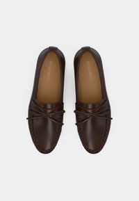 Σκούρα καφέ δερμάτινα loafers με στρογγυλερή μύτη, ραμμένες λεπτομέρειες και διακοσμητικό φιόγκο. Ομαλή υφή με μαλακό εσωτερικό πάτο.