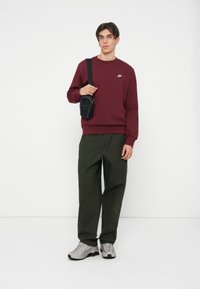 Bordový mikina s rebrovaným lemom, skombinovaná s olivovozelenými cargo nohavicami. Čierna crossbody taška pridáva jemné akcenty. Šedé tenisky dotvárajú vzhľad.