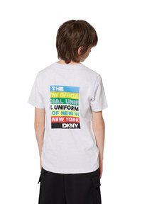 Camiseta de algodón blanca de manga corta con un diseño gráfico multicolor en la parte posterior, que muestra el texto y el logotipo de DKNY.