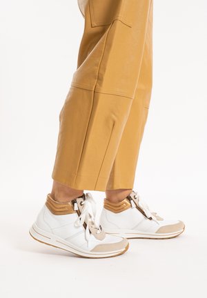 White and beige high-top sneakers with a textured upper, zip closure, and contrasting tan accents paired with mustard-colored cropped pants.