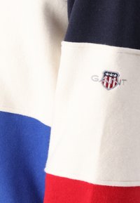 Farvet sweatshirt med blokke i marineblå, creme, kongeblå og rød. Broderet logo med skjolddesign på brystet. Blød tekstur.
