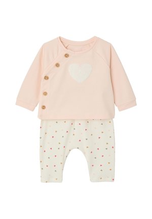 Weiches rosa Babyoberteil mit langen Ärmeln, Holzknöpfen und weißem Herz, kombiniert mit weißen Hosen, die mit kleinen mehrfarbigen Herzen verziert sind.