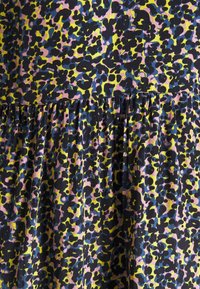 Gros plan sur un tissu avec couture froncée, présentant un motif léopard abstrait dans des couleurs noir, jaune, rose et bleu.