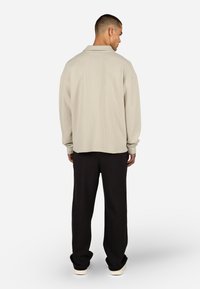 Világos bézs, texturált ing gallérral, bő fazonú és hosszú ujjú, sötét, bőszárú nadrággal és hétköznapi tornacipővel párosítva.