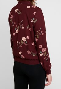 Veste bomber florale bordeaux avec des motifs de fleurs roses et vertes, poignets et ourlet côtelés, tissu doux, coupe décontractée et col montant.